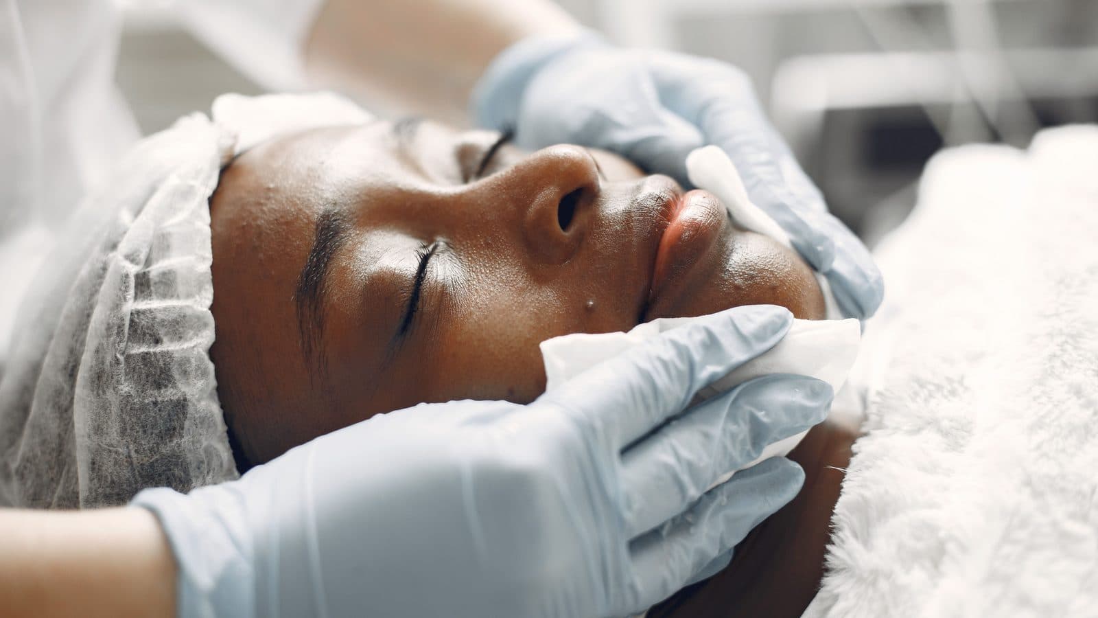 Gloved hands caring for a client's face during an in clinic treatment