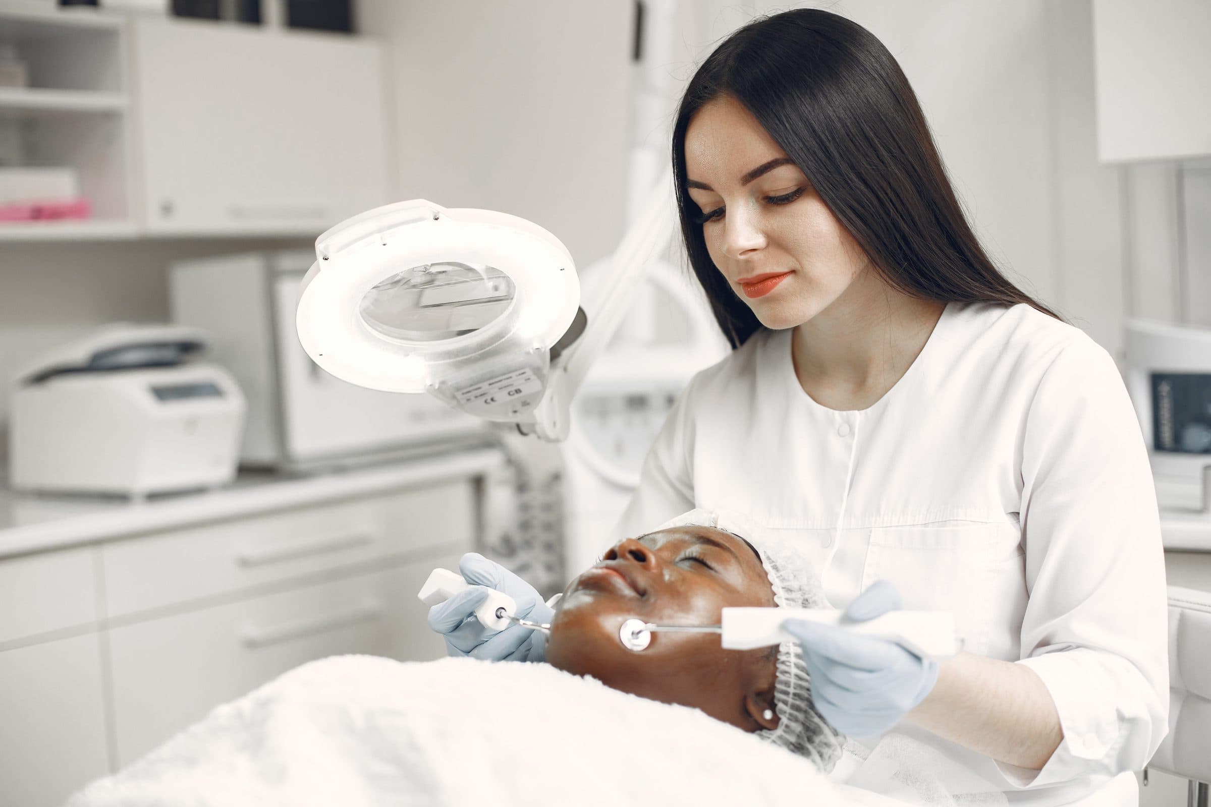 Skin specialist examining a client's face under a magnifier lamp